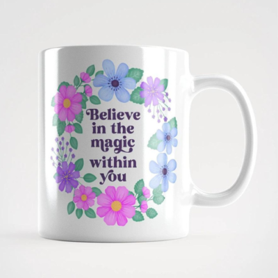 Motivational mug with quote: Believe in the magic withing you. Text with purple, blue and pink floral wreath with green leaves and foliage.