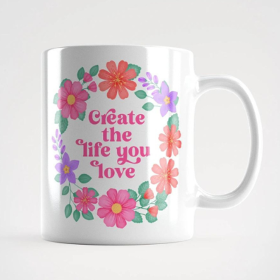 Motivational mug with quote: Create the life you love. Pink text with purple, pink and orange floral wreath with green leaves and foliage.