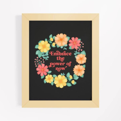 Motivational wall art with yellow and orange floral wreath on black background with text: Embrace the power of now.