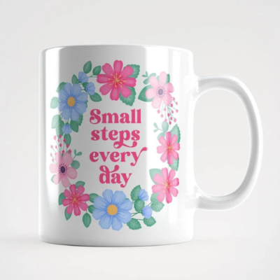 Motivational mug with quote: Small steps every day. Pink text with pink and blue floral wreath with green leaves and foliage.