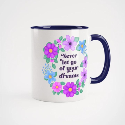 Motivational mug with quote: Never let go of your dreams. Text with blue and violet floral wreath with green leaves and foliage. White mug with deep indigo handle and mug inside color.